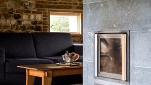 A cozy room with a stone wall, a dark sofa, a wooden table with a teapot, and a fireplace.