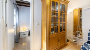 A room with a wooden wardrobe, a bedside table with a lamp, and a mirror on the wall.