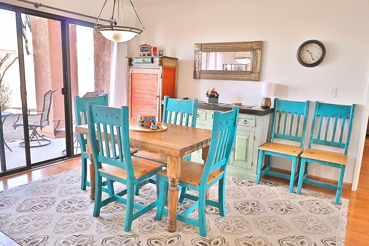 A dining area with a wooden table and turquoise chairs, a kitchen with teal cabinets, and a large mirror on the wall.