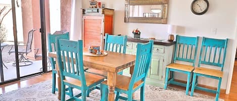 A dining area with a wooden table and turquoise chairs, a kitchen with teal cabinets, and a large mirror on the wall.