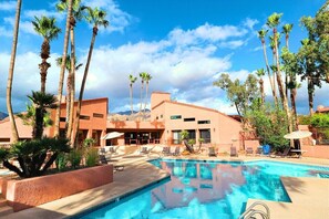 A swimming pool surrounded by palm trees and lounge chairs, with a building in the background.