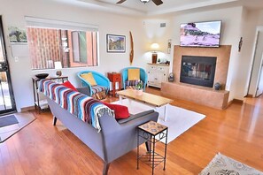 A living room with a sofa, armchairs, a coffee table, a fireplace, and a television mounted above it.