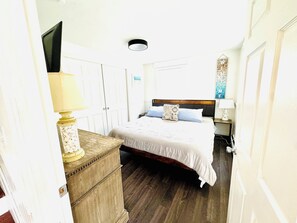 Une chambre à coucher avec un lit, des tables de chevet, une commode, un téléviseur et une porte.