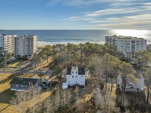 Zona residencial costeira com vários edifícios de apartamentos, um parque de estacionamento e uma praia ao fundo.