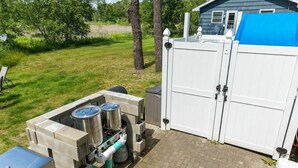 En portabel matlagningsplats med en grill och förvaringsbehållare, ett vitt staket och ett hus i bakgrunden.
