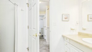 Un baño con tocador blanco, un espejo grande y una puerta que da a un pasillo.