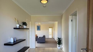 Un couloir avec un tapis bleu, une porte blanche et un salon à l’arrière-plan.