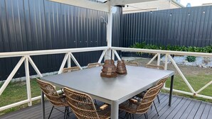 Une terrasse extérieure couverte, avec une table et des chaises en osier.