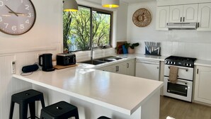 Une cuisine moderne dotée d’un îlot central, de meubles blancs, d’une grande fenêtre et de luminaires suspendus.
