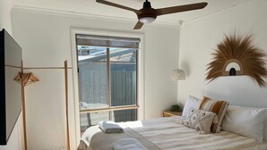Une chambre avec un grand lit, un ventilateur de plafond, une fenêtre et un élément décoratif mural.
