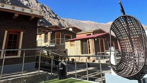 Een gebouw met een trap die leidt naar een balkon, een metalen sculptuur en een bergachtig landschap op de achtergrond.
