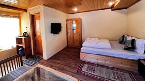 Een knus vertrek met houten plafond en wanden, een bed met kussens, een televisie aan de muur en een klein tafeltje met een waterkoker.