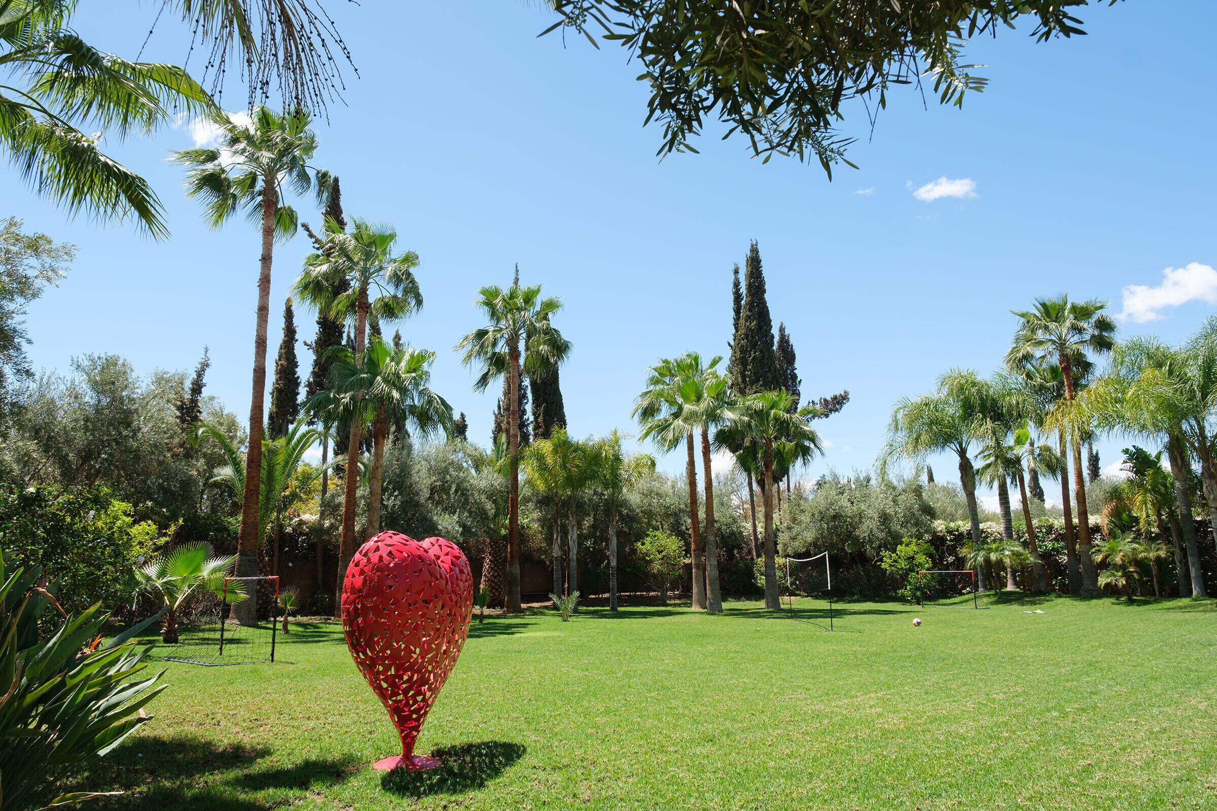 Un jardin bien entretenu, agrémenté de différentes espèces de palmiers et orné d’une sculpture rouge remarquable, placée en premier plan.