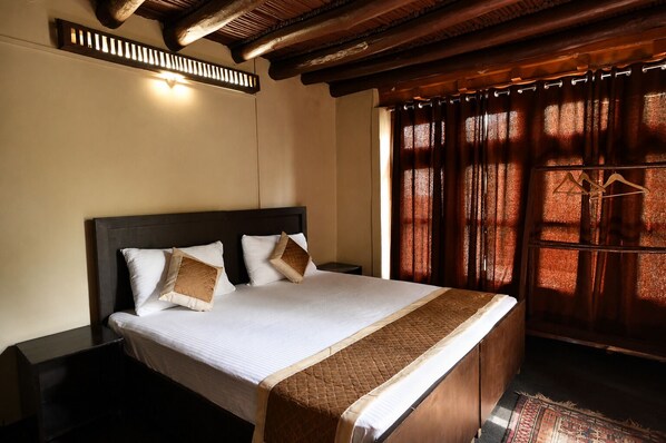 A hotel room with a large bed, wooden headboard, and a window with patterned curtains. - House Of Stok (Leh)