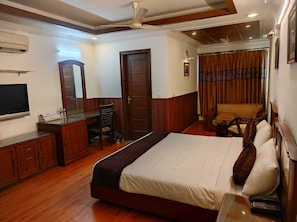 A hotel room with a bed, a desk with a chair, a television, a wardrobe, and a ceiling fan. - Residency Stay INN (New Delhi)