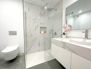 Un baño moderno con inodoro, ducha con mampara de vidrio y tocador con lavabo y espejo.