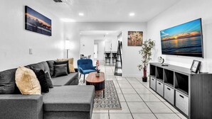 Una sala de estar moderna con un sofá seccional gris, un sillón azul, una mesa de centro y un televisor sobre un mueble de madera.