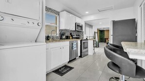 Una cocina moderna con armarios blancos, un refrigerador de acero inoxidable, un microondas y una estación para café.