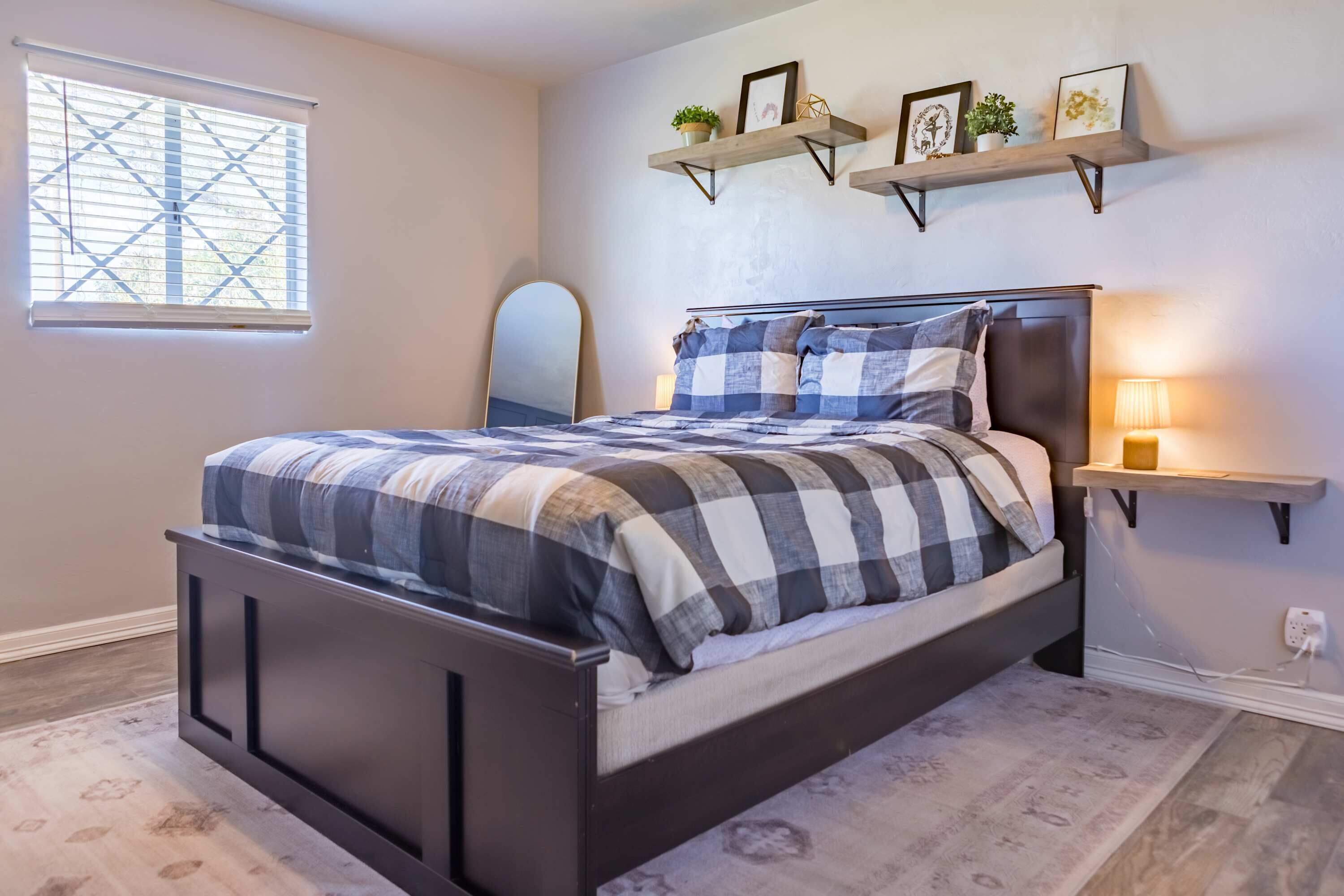 A bedroom with a bed, a window, and wall-mounted shelves with decorative items.