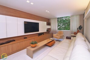 A modern living room with a flat-screen TV, a sofa, a coffee table, and a window with curtains. - Aristides Leblon (Rio de Janeiro)
