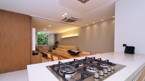 A modern kitchen with a gas stove, a dining area with a sofa, and a view of greenery outside. - Aristides Leblon (Rio de Janeiro)