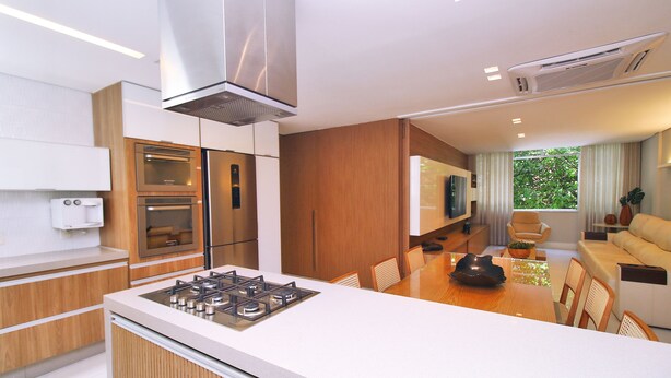 A modern kitchen with a gas stove, built-in oven, and microwave. There is a dining area with a table and chairs, and a living room with a sofa and a TV. - Aristides Leblon (Rio de Janeiro)