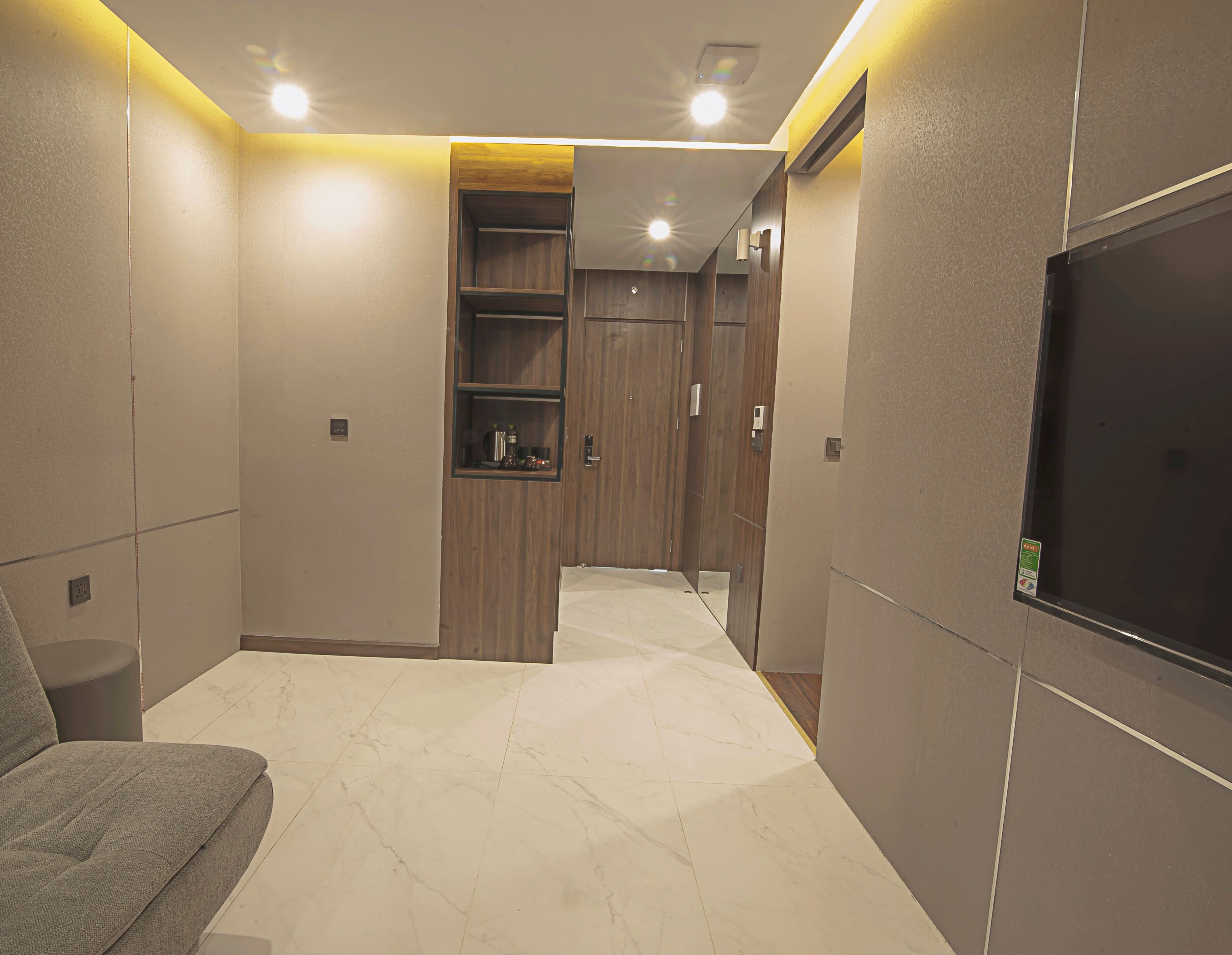A hotel room with a sofa, a TV, a wooden wardrobe, and a marble floor.