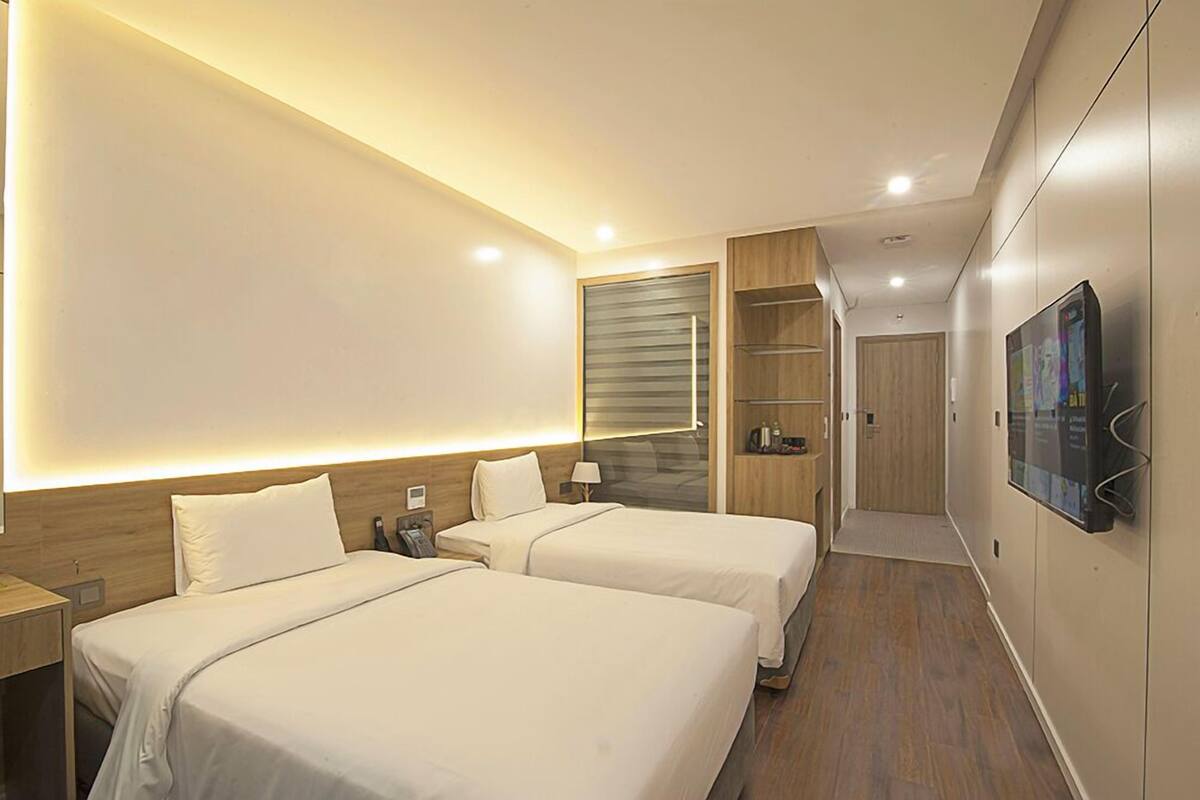 A hotel room with two beds, a TV, a wooden wardrobe, and a small desk.