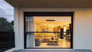 A modern living room with a sofa, coffee table, and dining area visible through a glass door. - Elmima Villa  (Mylopotamos)