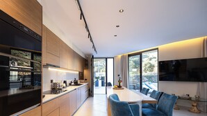 A modern kitchen with built-in appliances, a dining area with blue chairs, and a large window offering a view of the outdoors. - Elmima Villa  (Mylopotamos)