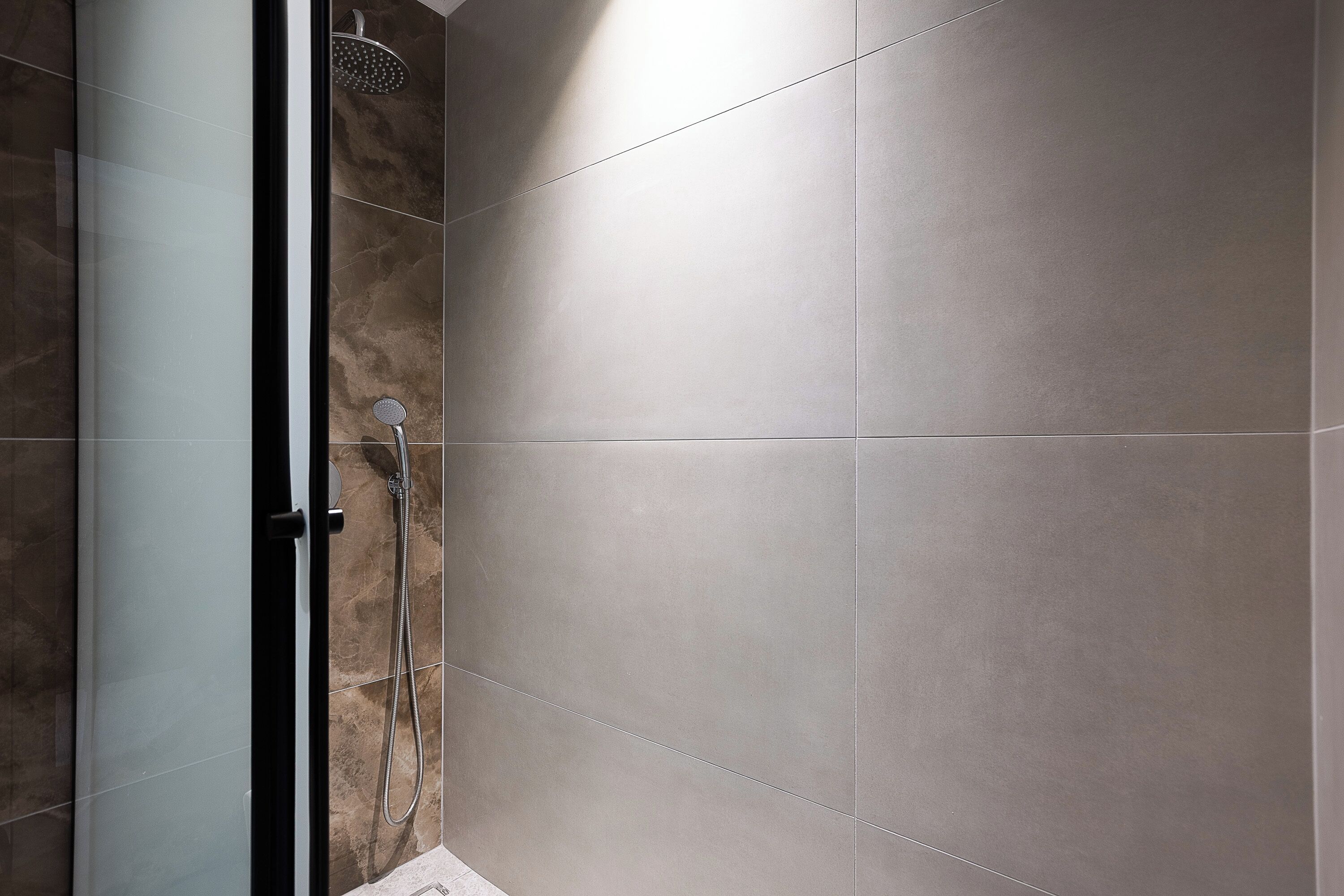 Un espace douche moderne doté d’une porte en verre, d’un pommeau de douche à main et d’un robinet mural.