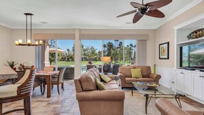 A spacious living room with a large TV, comfortable seating, a ceiling fan, and a view of the outdoors. - Casa Solara | PGA West Pool, Spa & Firepit (La Quinta)