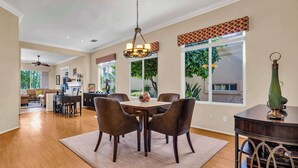 A spacious dining area with a wooden table and chairs, large windows with decorative valances, and a ceiling fan. - Casa Solara | PGA West Pool, Spa & Firepit (La Quinta)