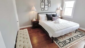 Ein Schlafzimmer mit einem Bett, Nachttischen, einer Bank, einem Teppich und gerahmten Bildern an der Wand.