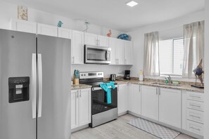 A modern kitchen with white cabinets, stainless steel appliances, and a window with curtains.