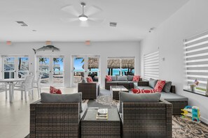 A spacious living area with wicker furniture, a ceiling fan, and large windows offering a view of the beach.