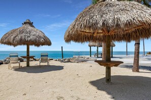 A beach with thatched umbrellas, lounge chairs, and a clear view of the sea.