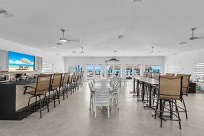 A spacious dining area with high tables and chairs, large windows with ocean views, and ceiling fans.