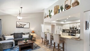 A modern living room with a sofa, coffee table, and a dining area with chairs and a kitchen in the background.