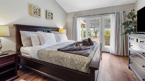 A bedroom with a large bed, a nightstand, a dresser, and a television.