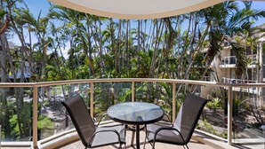 A balcony with a glass balustrade, two chairs, and a round table.