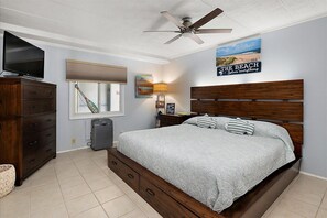 Quarto com cama, penteadeira, ventilador de teto, televisão, janela, luminária e obras de arte.