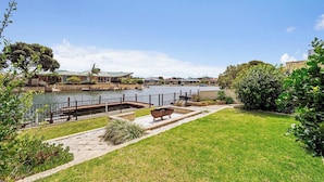 A grassy area with a dock and a boat, a building with a green roof, and a clear sky. - Canal view • Pet friendly • Private Jetty • Spacious Yard (South Yunderup)