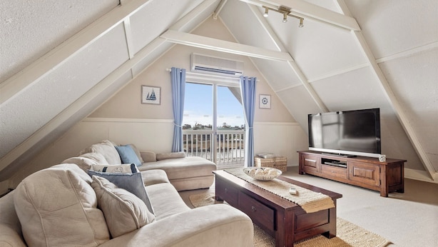 A cozy attic room with a large window, a sofa, a TV, and a wooden cabinet. - Canal view • Pet friendly • Private Jetty • Spacious Yard (South Yunderup)