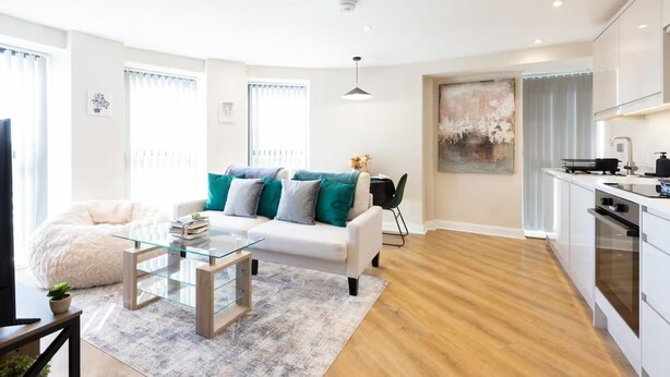 Un salon moderne avec un canapé blanc, des coussins turquoise, une table basse en verre et un plancher en bois.