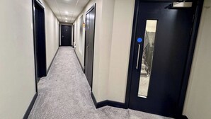 Un couloir d’hôtel avec des portes, un sol recouvert de moquette et un panneau indiquant la sortie de secours.