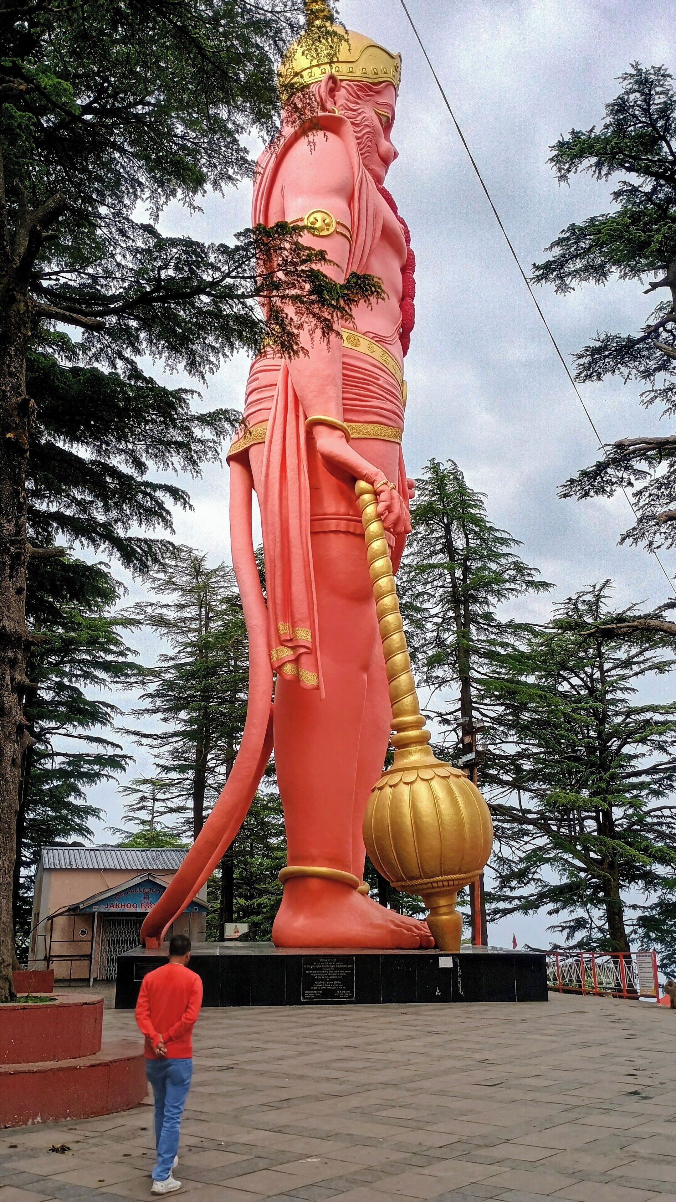 A large statue of a figure holding a golden staff, standing on a paved area with trees in the background.