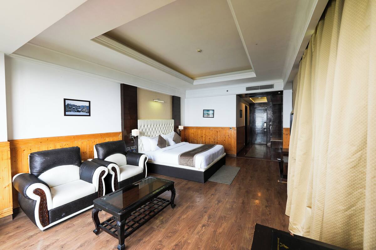A hotel room with a bed, two sofas, a coffee table, and a wooden floor.