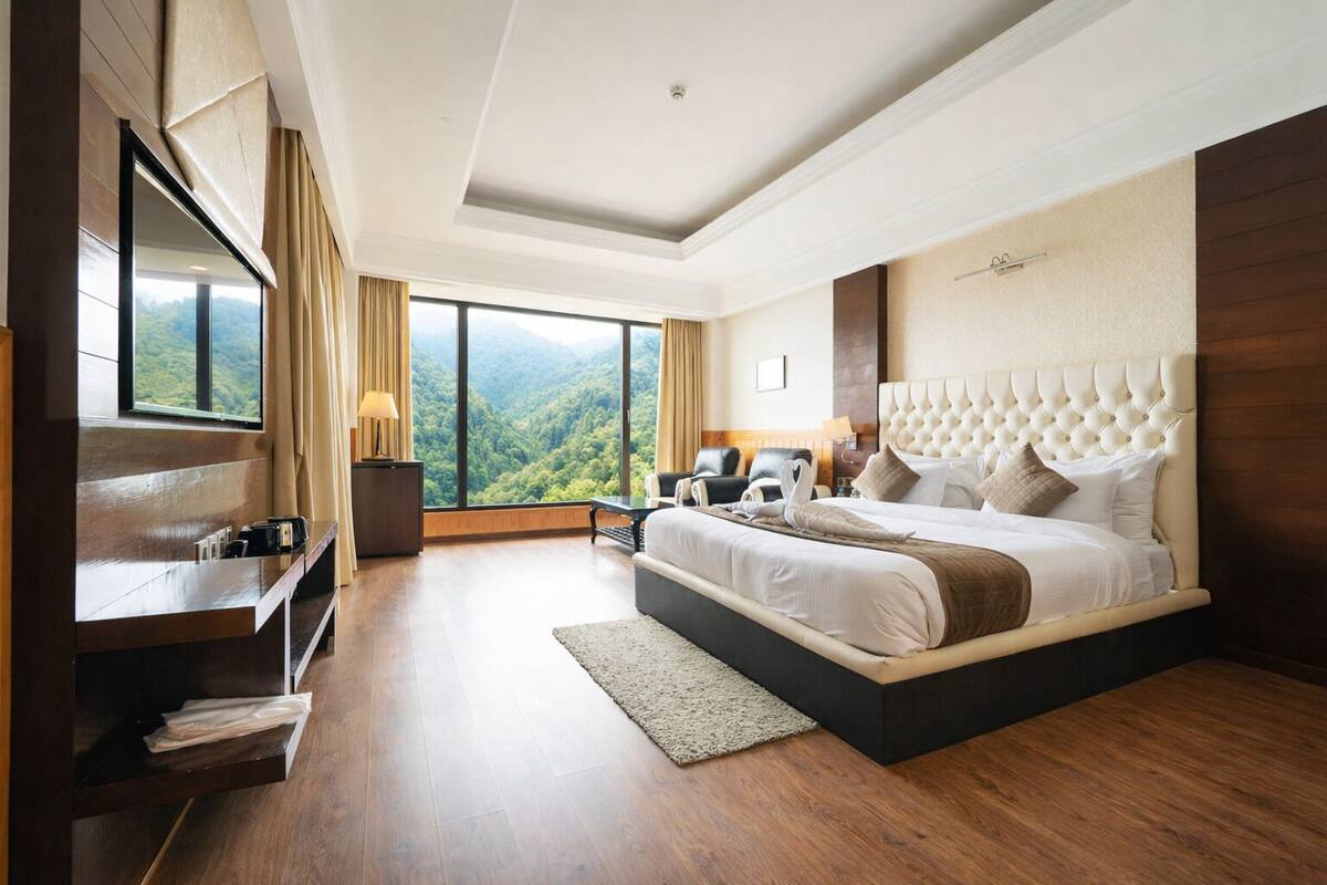 A modern hotel room with a large bed, a desk, and a view of a forested landscape.
