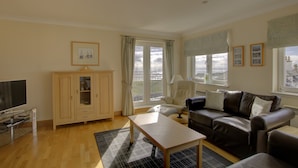 A living room with a sofa, a coffee table, a TV, and a cabinet. - Top-floor, two-bedroom golf apartment with views over the famous James Braid Brora Golf Course (Brora)